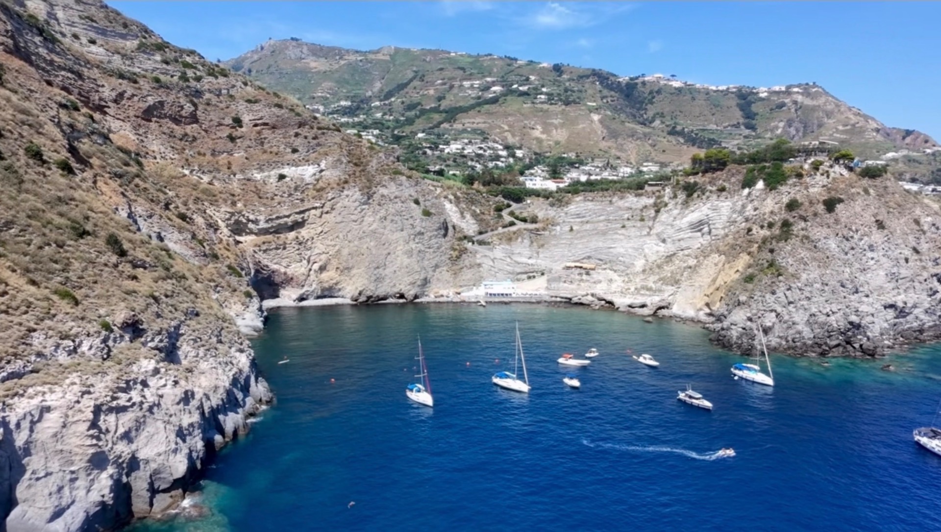 Bagnanti nuotano e si tuffano in mare limpido tra rocce, con gommoni e scivoli verdi.