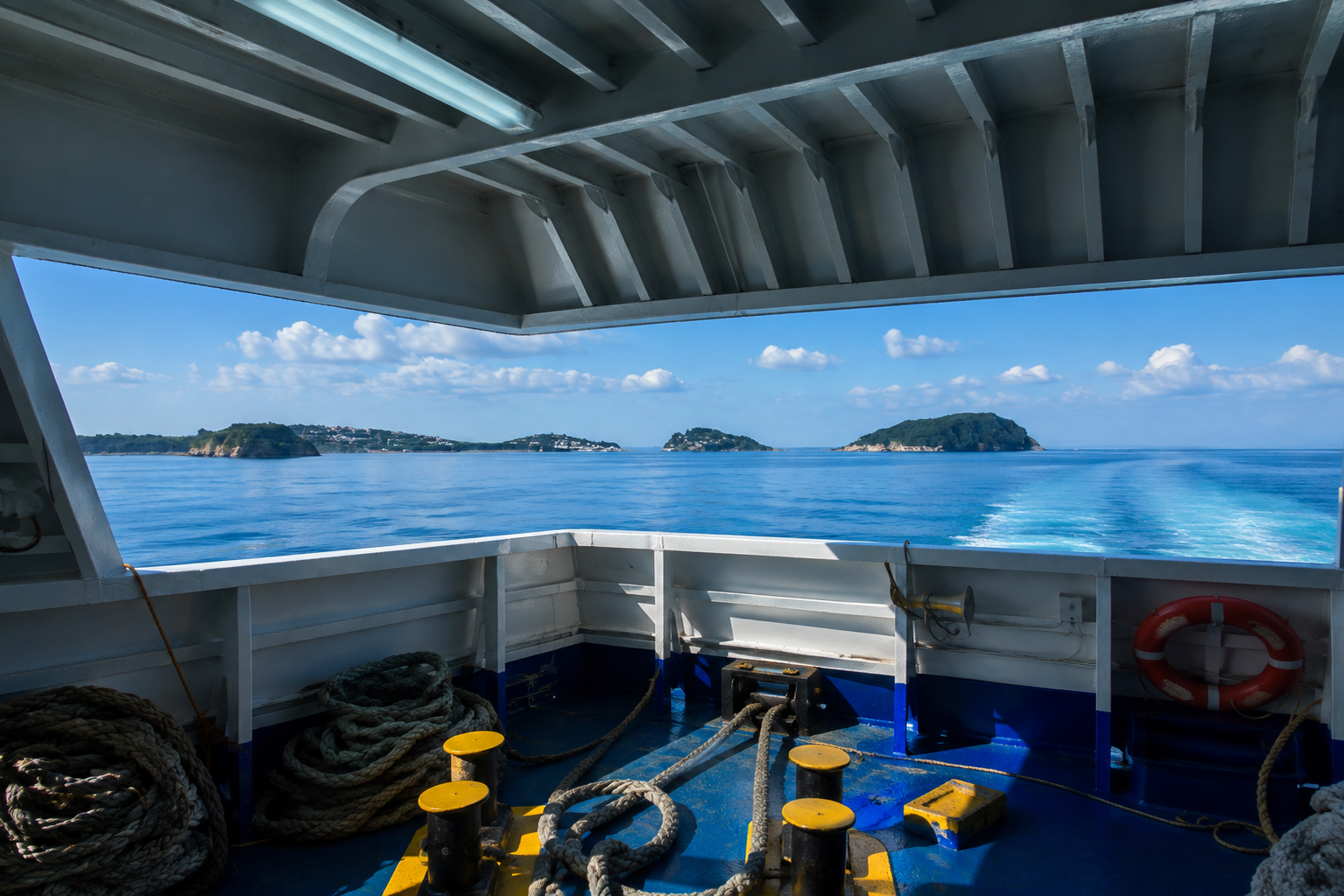 Cabina di nave con corde e salvagente, vista sul mare blu e coste verdi sotto cielo nuvoloso.